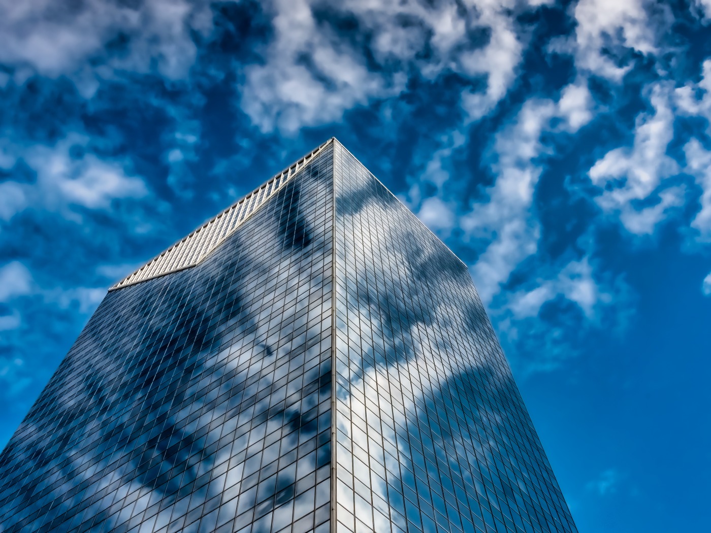 Glass corporate tower seen from below against a cloudy sky